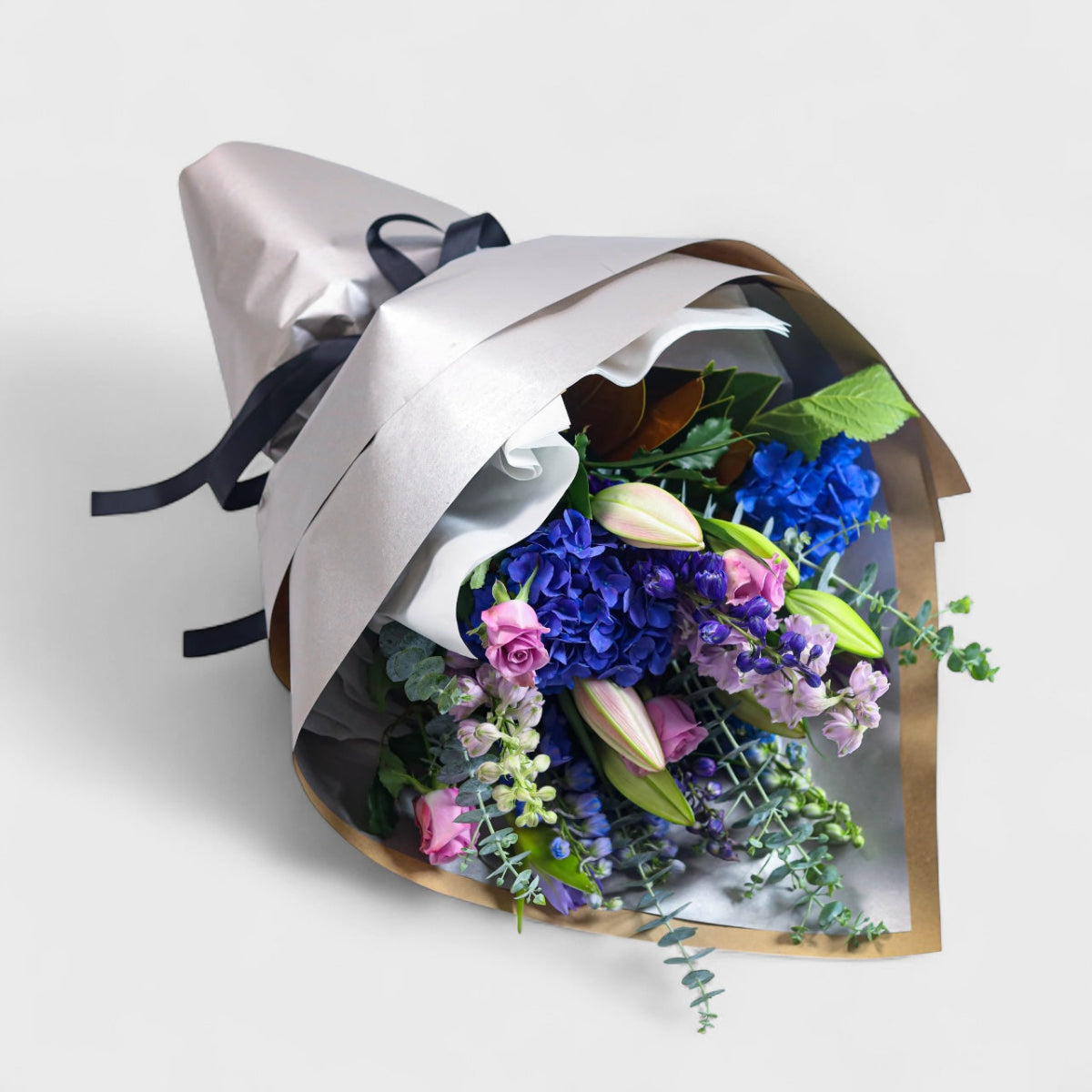 Bouquet of blue and purple flowers wrapped in metallic paper with a black ribbon on a light gray background