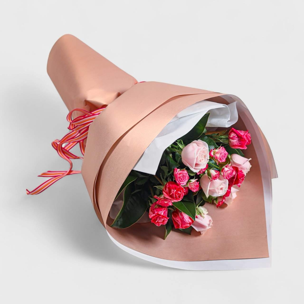 Bouquet of pink and red flowers wrapped in rosegold paper with a ribbon
